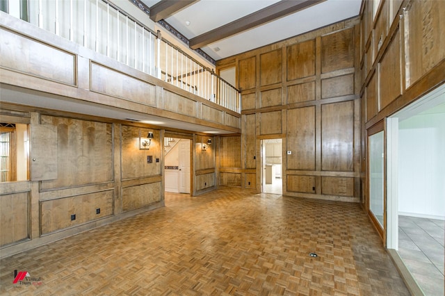 interior space featuring beamed ceiling, a high ceiling, parquet floors, and wood walls