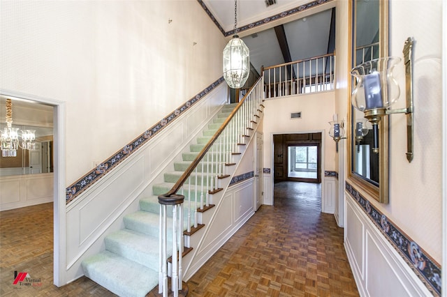 stairway featuring crown molding, parquet flooring, a towering ceiling, and a notable chandelier