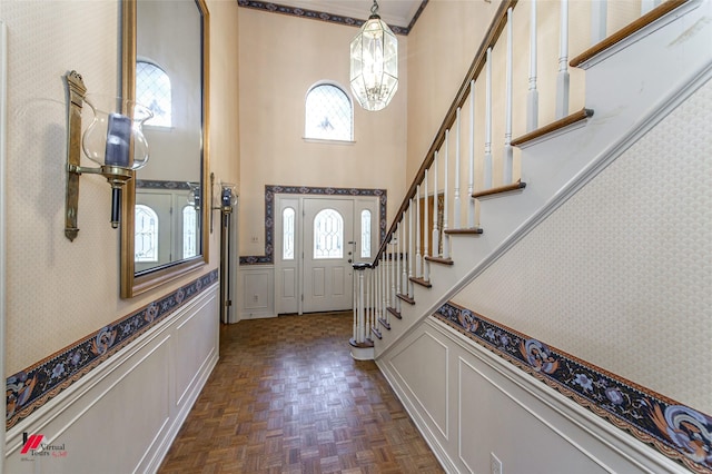 foyer featuring crown molding, a notable chandelier, dark parquet flooring, and a towering ceiling