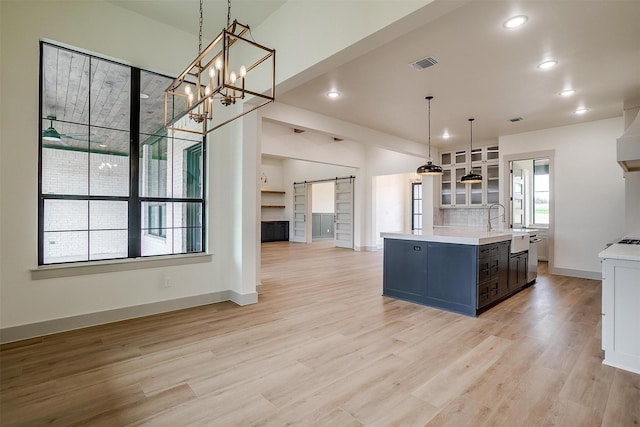 kitchen featuring sink, tasteful backsplash, light wood-type flooring, pendant lighting, and a barn door