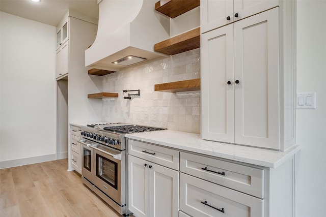 kitchen featuring white cabinetry, double oven range, backsplash, light stone counters, and custom range hood