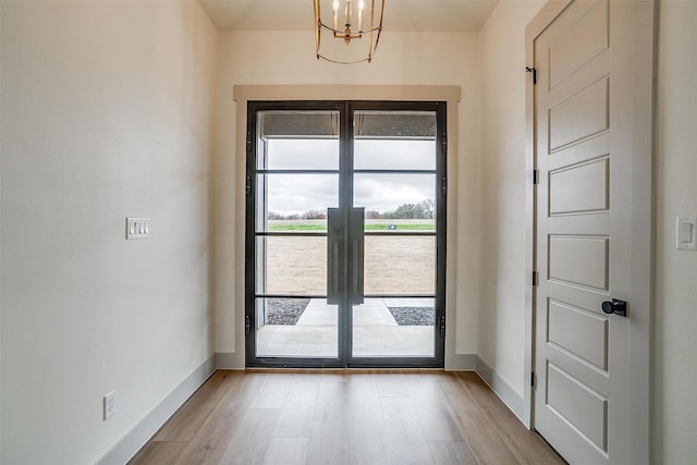 doorway with a notable chandelier, french doors, and light wood-type flooring