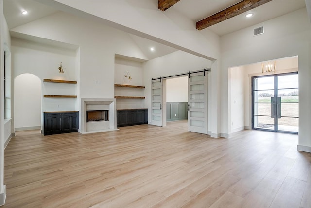 unfurnished living room featuring beamed ceiling, a barn door, high vaulted ceiling, and light hardwood / wood-style floors