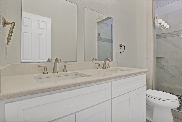 bathroom featuring toilet, double vanity, a sink, and a marble finish shower