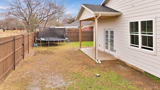 view of yard featuring french doors, a trampoline, and a fenced backyard