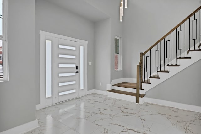 foyer featuring marble finish floor, stairway, and baseboards