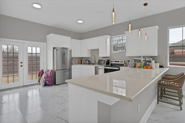 kitchen featuring stainless steel appliances, a peninsula, marble finish floor, light countertops, and decorative light fixtures