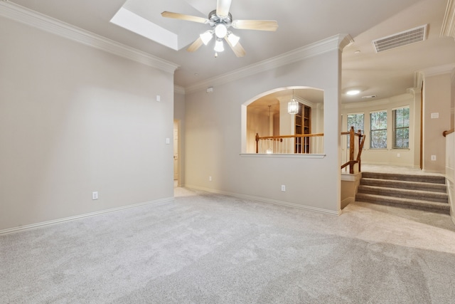 unfurnished living room with ceiling fan, light colored carpet, ornamental molding, and a skylight