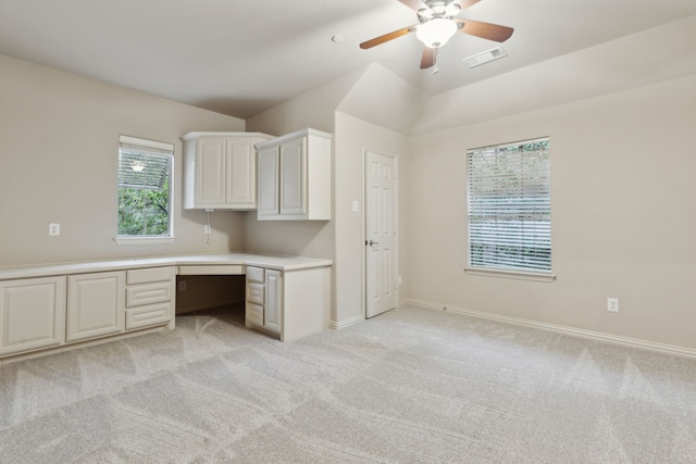 unfurnished office with built in desk, light colored carpet, ceiling fan, and vaulted ceiling