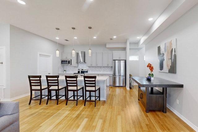 kitchen with a kitchen breakfast bar, decorative backsplash, hanging light fixtures, stainless steel appliances, and wall chimney range hood