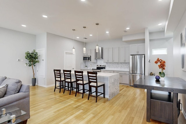 kitchen featuring wall chimney exhaust hood, a center island with sink, a kitchen breakfast bar, pendant lighting, and stainless steel appliances