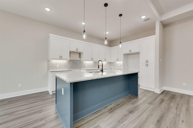 kitchen featuring sink, white cabinetry, tasteful backsplash, light wood-type flooring, and a kitchen island with sink