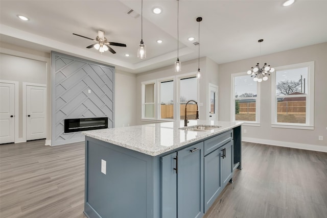 kitchen with sink, light stone countertops, a large fireplace, a center island with sink, and decorative light fixtures