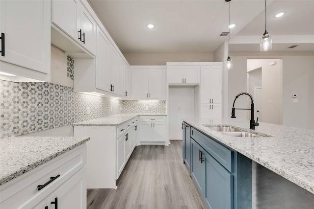 kitchen featuring sink, white cabinetry, tasteful backsplash, pendant lighting, and light stone countertops