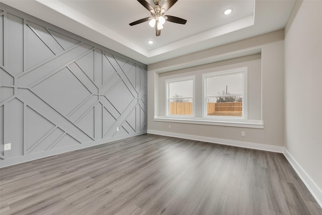 empty room featuring ceiling fan, a raised ceiling, and light hardwood / wood-style flooring