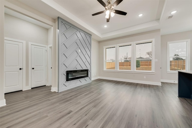 unfurnished living room with a tray ceiling, a premium fireplace, ceiling fan, and light wood-type flooring