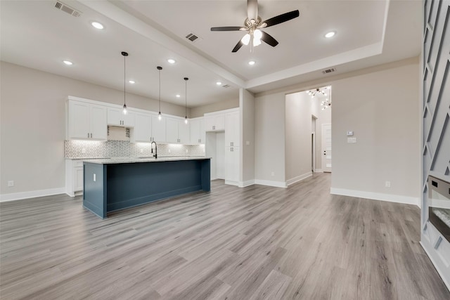 kitchen with white cabinetry, pendant lighting, light hardwood / wood-style floors, and an island with sink