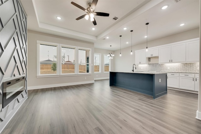 kitchen with hanging light fixtures, tasteful backsplash, an island with sink, white cabinets, and a raised ceiling