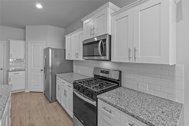 kitchen with white cabinetry, tasteful backsplash, light stone counters, light wood-type flooring, and stainless steel appliances