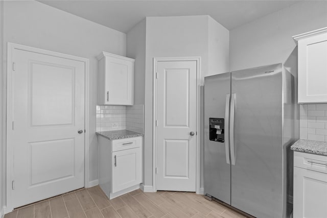 kitchen with backsplash, stainless steel fridge, light stone countertops, and white cabinets