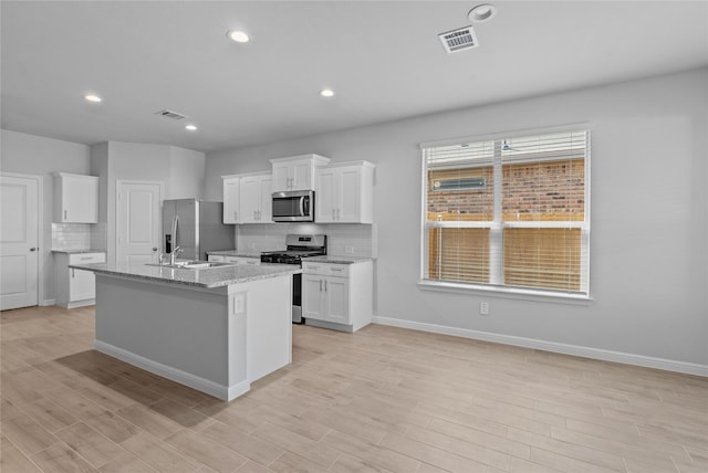 kitchen featuring white cabinetry, decorative backsplash, stainless steel appliances, light stone countertops, and a center island with sink