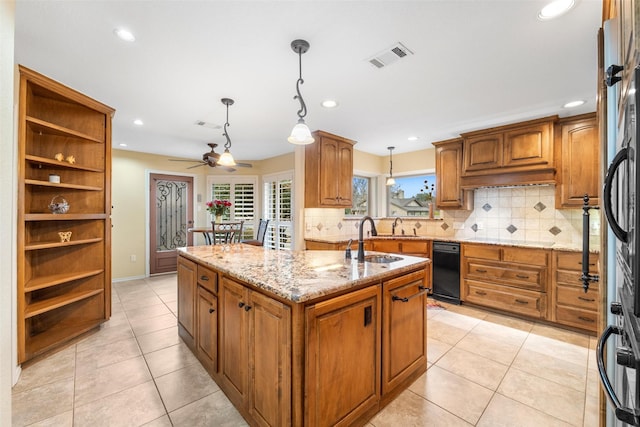 kitchen featuring sink, hanging light fixtures, backsplash, light stone countertops, and an island with sink