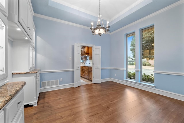 unfurnished dining area with a chandelier, a tray ceiling, dark hardwood / wood-style flooring, and crown molding