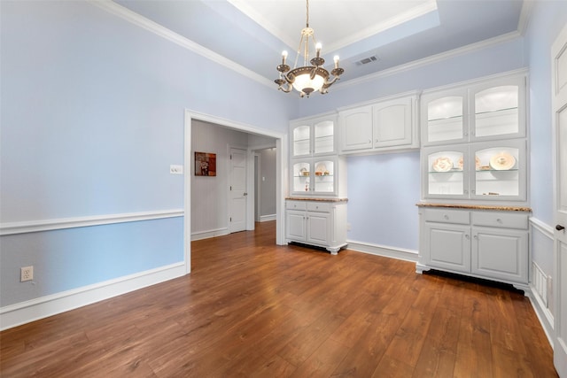 unfurnished dining area with dark wood-type flooring, crown molding, a raised ceiling, and a notable chandelier