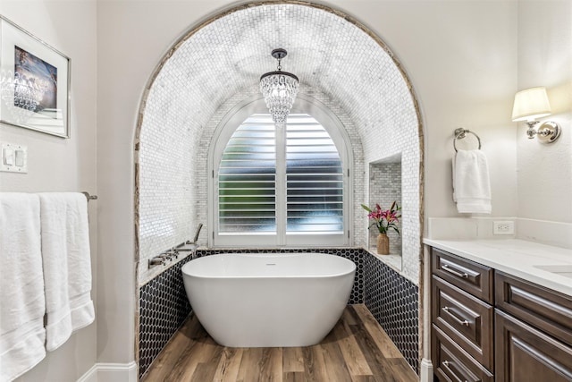 full bath featuring a soaking tub, wood finished floors, vanity, and a notable chandelier