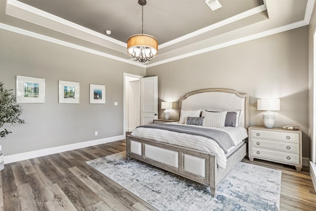 bedroom featuring a raised ceiling, visible vents, baseboards, and wood finished floors