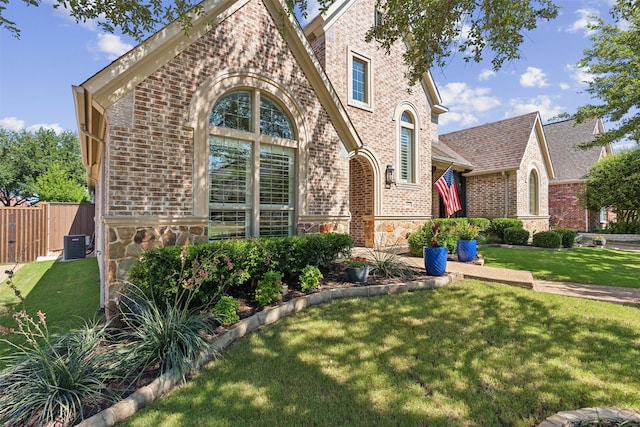 view of front of house featuring central AC unit, brick siding, fence, stone siding, and a front lawn