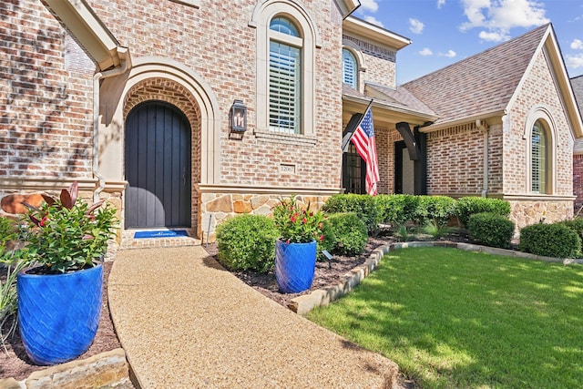 property entrance with stone siding, a shingled roof, a lawn, and brick siding