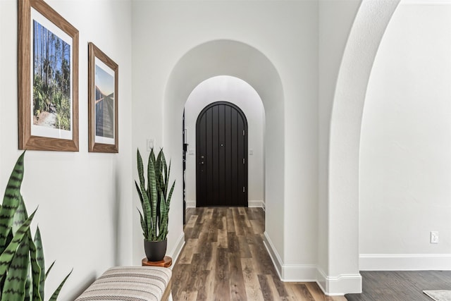 foyer entrance featuring arched walkways, baseboards, and wood finished floors