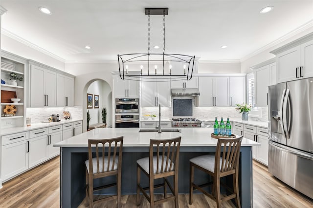 kitchen featuring arched walkways, a kitchen island with sink, stainless steel appliances, a sink, and light countertops