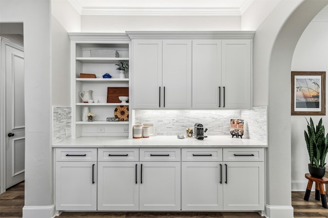 bar with arched walkways, decorative backsplash, dark wood-style flooring, and ornamental molding