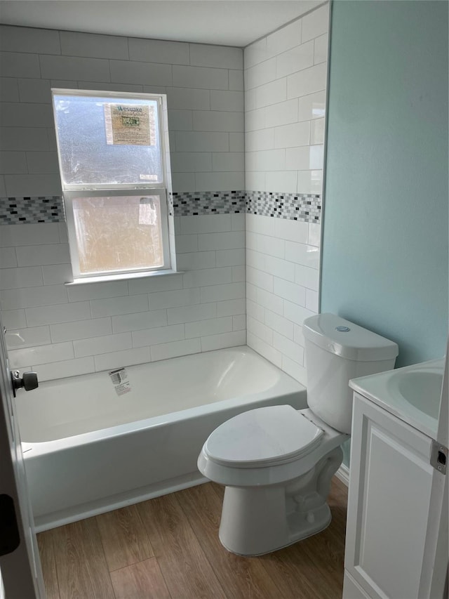 full bathroom with hardwood / wood-style flooring, tiled shower / bath, vanity, and toilet