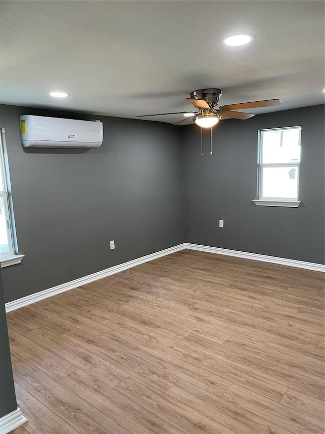 unfurnished room featuring an AC wall unit, ceiling fan, and light wood-type flooring