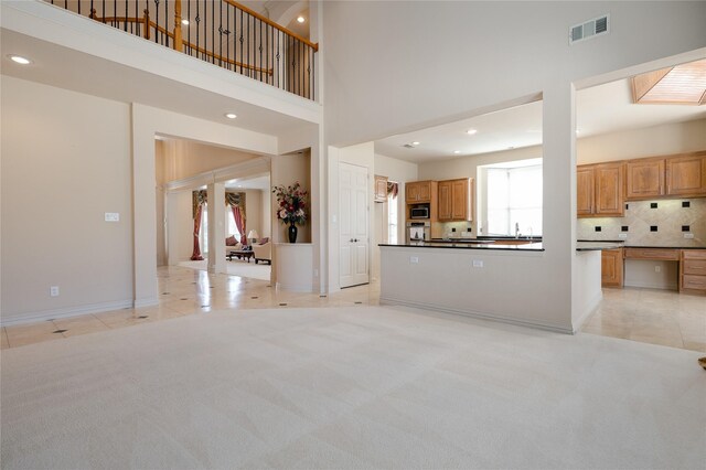 unfurnished living room featuring light carpet, a towering ceiling, visible vents, and light tile patterned flooring