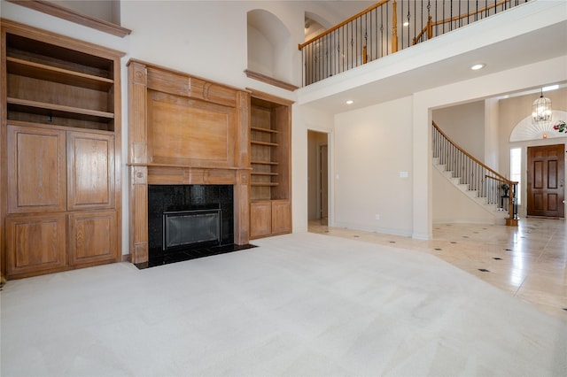 unfurnished living room featuring a high end fireplace, light carpet, and a towering ceiling