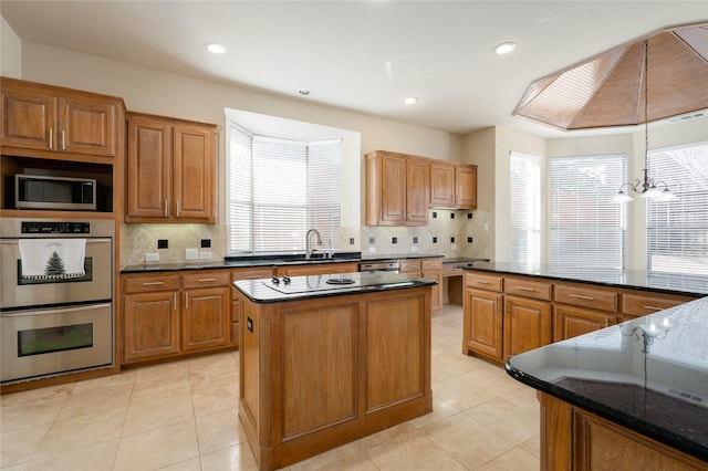 kitchen with appliances with stainless steel finishes, brown cabinetry, a kitchen island, and hanging light fixtures