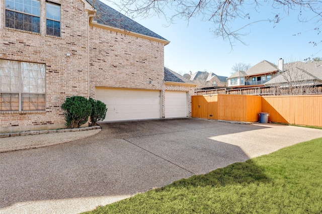 view of side of property with a shingled roof, brick siding, fence, and driveway