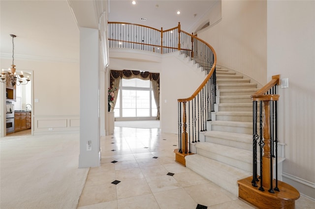 entrance foyer with ornamental molding, a decorative wall, a towering ceiling, and a notable chandelier