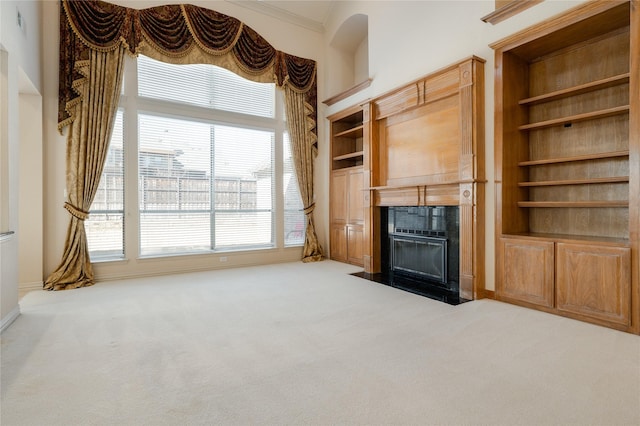 unfurnished living room featuring a towering ceiling, ornamental molding, carpet floors, built in shelves, and a fireplace