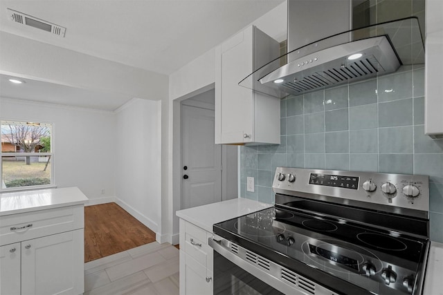 kitchen with electric stove, white cabinetry, wall chimney exhaust hood, and tasteful backsplash