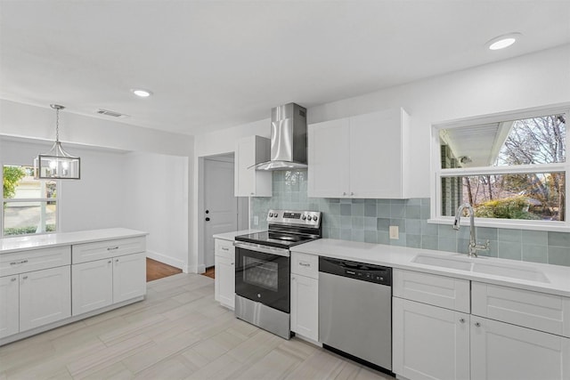 kitchen with appliances with stainless steel finishes, pendant lighting, white cabinetry, sink, and wall chimney exhaust hood