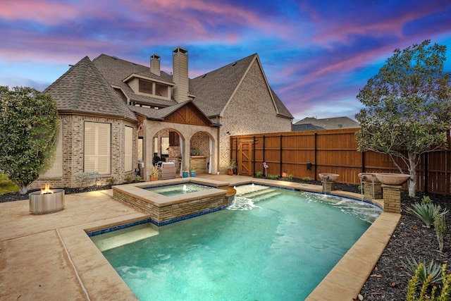 pool at dusk featuring an in ground hot tub, pool water feature, an outdoor fire pit, and a patio area