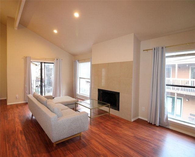 living room featuring a tiled fireplace, dark wood-type flooring, and vaulted ceiling