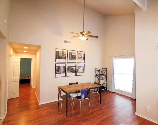 dining area with ceiling fan, dark hardwood / wood-style floors, and a high ceiling