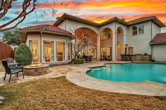 back house at dusk with an outdoor fire pit, a fenced in pool, and a patio area