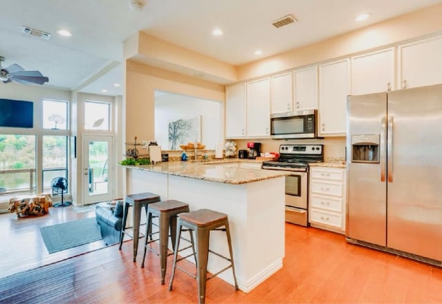 kitchen featuring a breakfast bar, light wood finished floors, visible vents, white cabinets, and appliances with stainless steel finishes